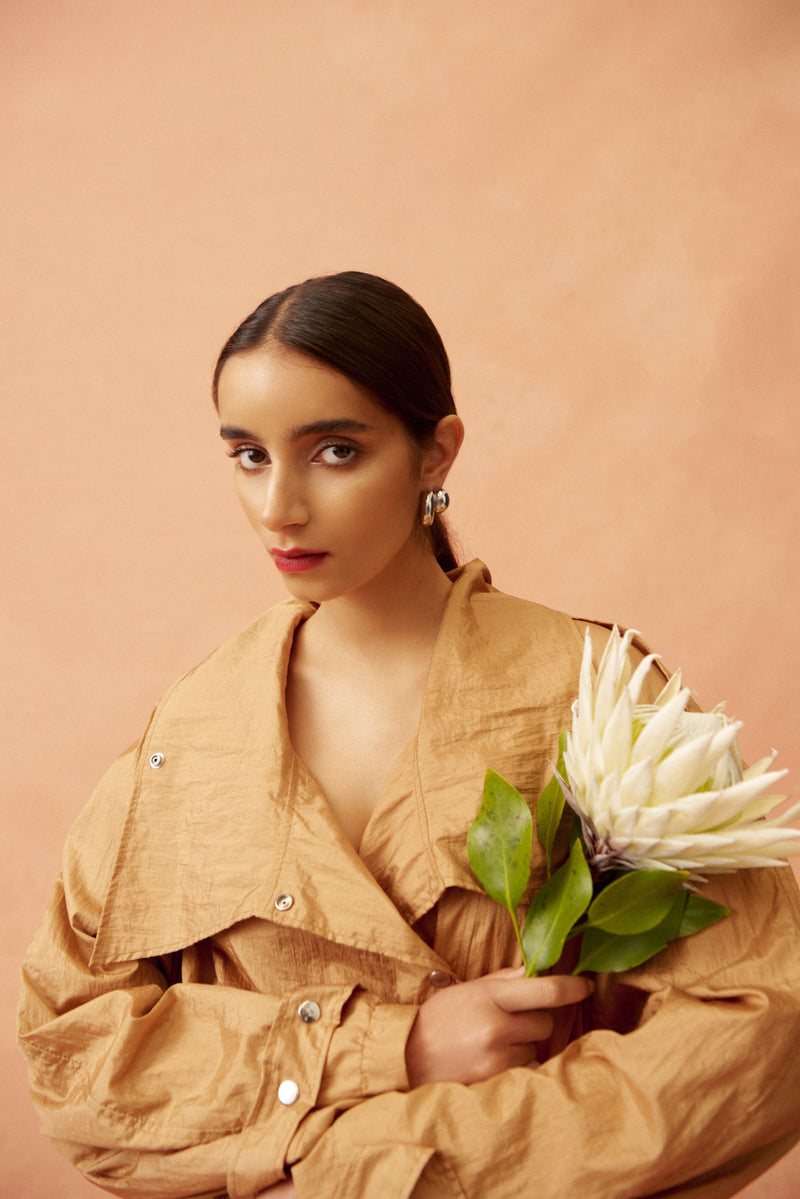 Woman in a beige jacket holding flowers against a peach background